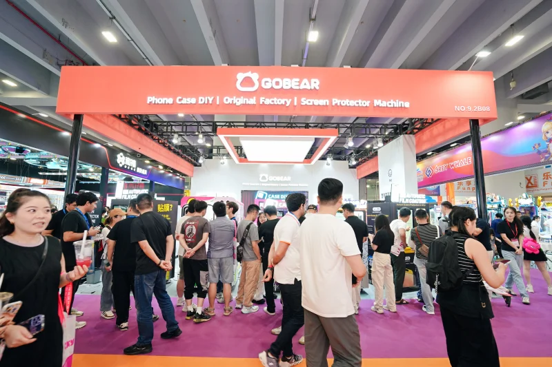 GOBEAR exhibition booth showcasing phone case DIY machines and screen protector equipment at trade show, with visitors gathered around the orange-branded display
