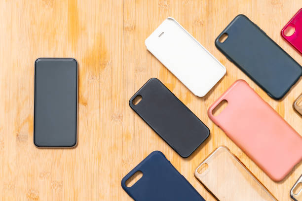 Pile of multicolored plastic back covers for mobile phones on wooden background with a phone on the side
